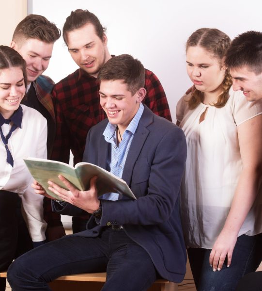 Young people studying with books on white desk. Beautiful girls and guys working together wearing casual clothes.