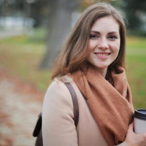 Portrait of a smiling woman holding a coffee cup in a serene autumn park setting.